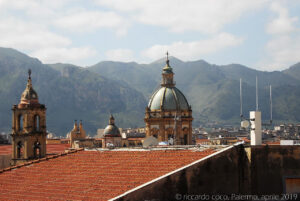 Verso sud – ovest, da destra verso sinistra la cupola di Casa Professa, e il campanile con le bandiere, quest’ultimo dopo la cupola della chiesa del Carmine Maggiore ed infine la torre di palazzo Marchesi.